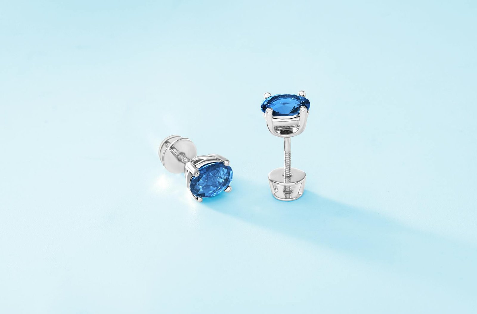 Luxurious silver stud earrings with blue gemstones on a soft blue background.