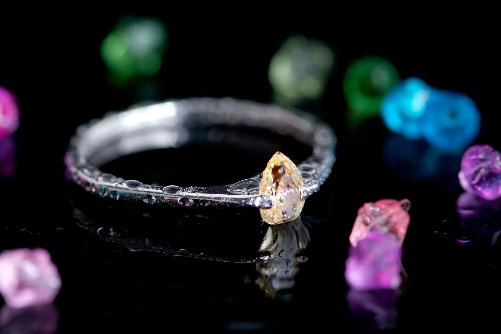 A stunning diamond ring set against colorful gemstones on a reflective surface.