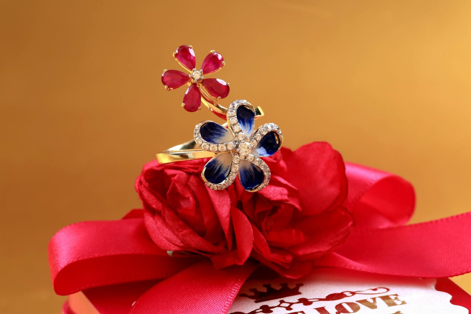 Close-up of floral design rings on a red ribbon gift box with vibrant flowers.