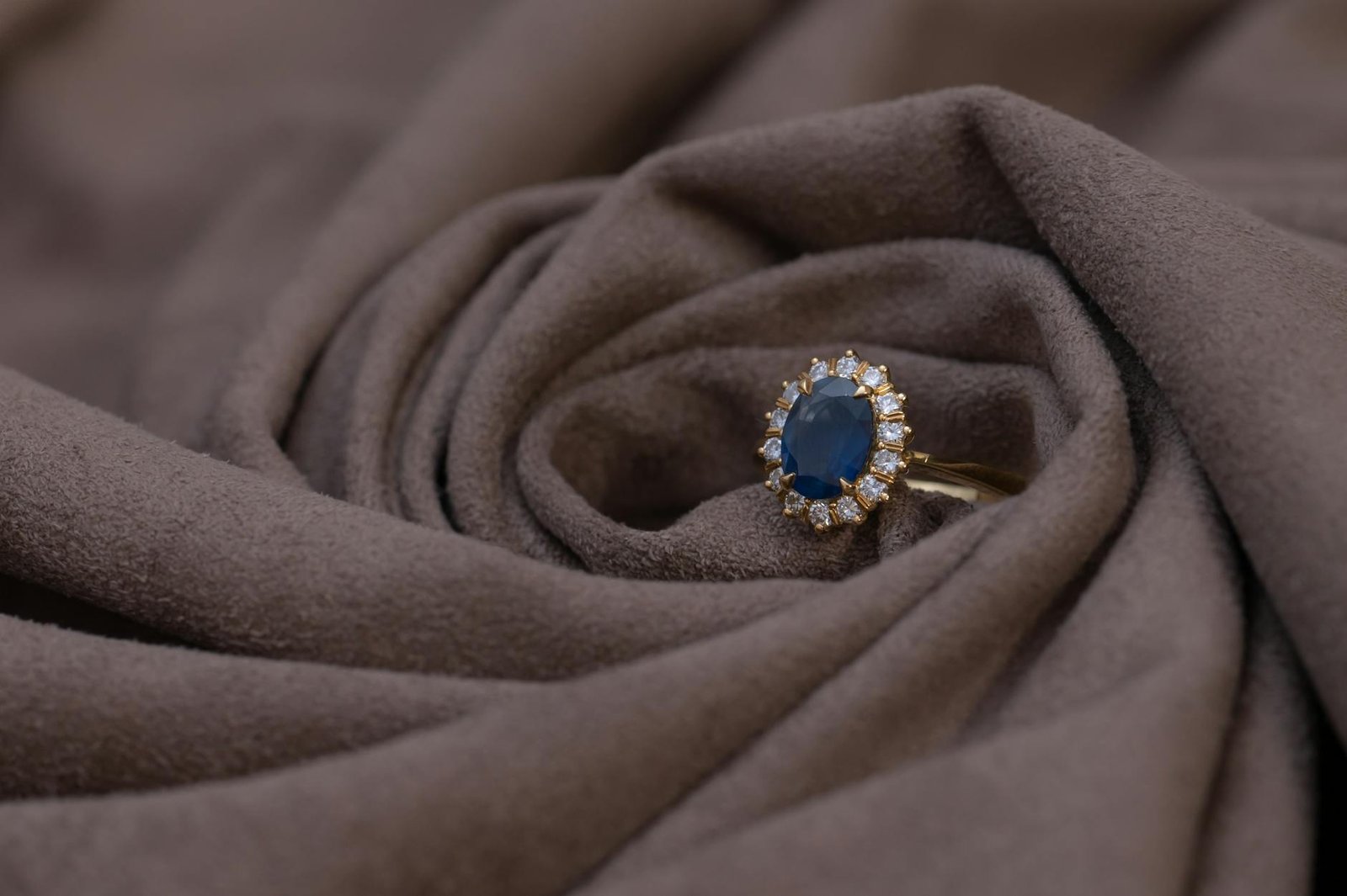 Close-up of a sapphire and diamond gold ring on brown suede, highlighting luxury jewelry details.