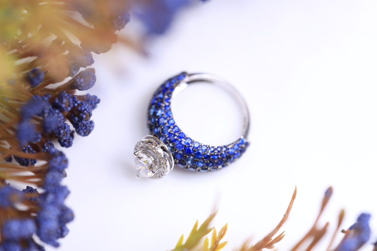 Close-up of a silver ring adorned with blue sapphires and floral motifs on a white background.