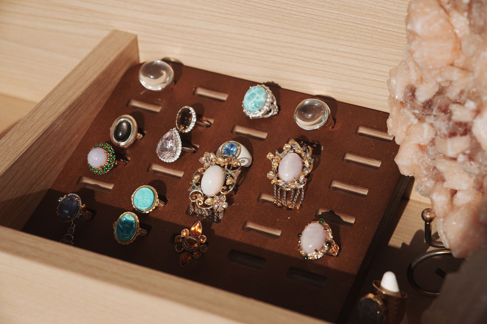 A neatly organized jewelry box showcasing various gemstone rings with a natural crystal accent.