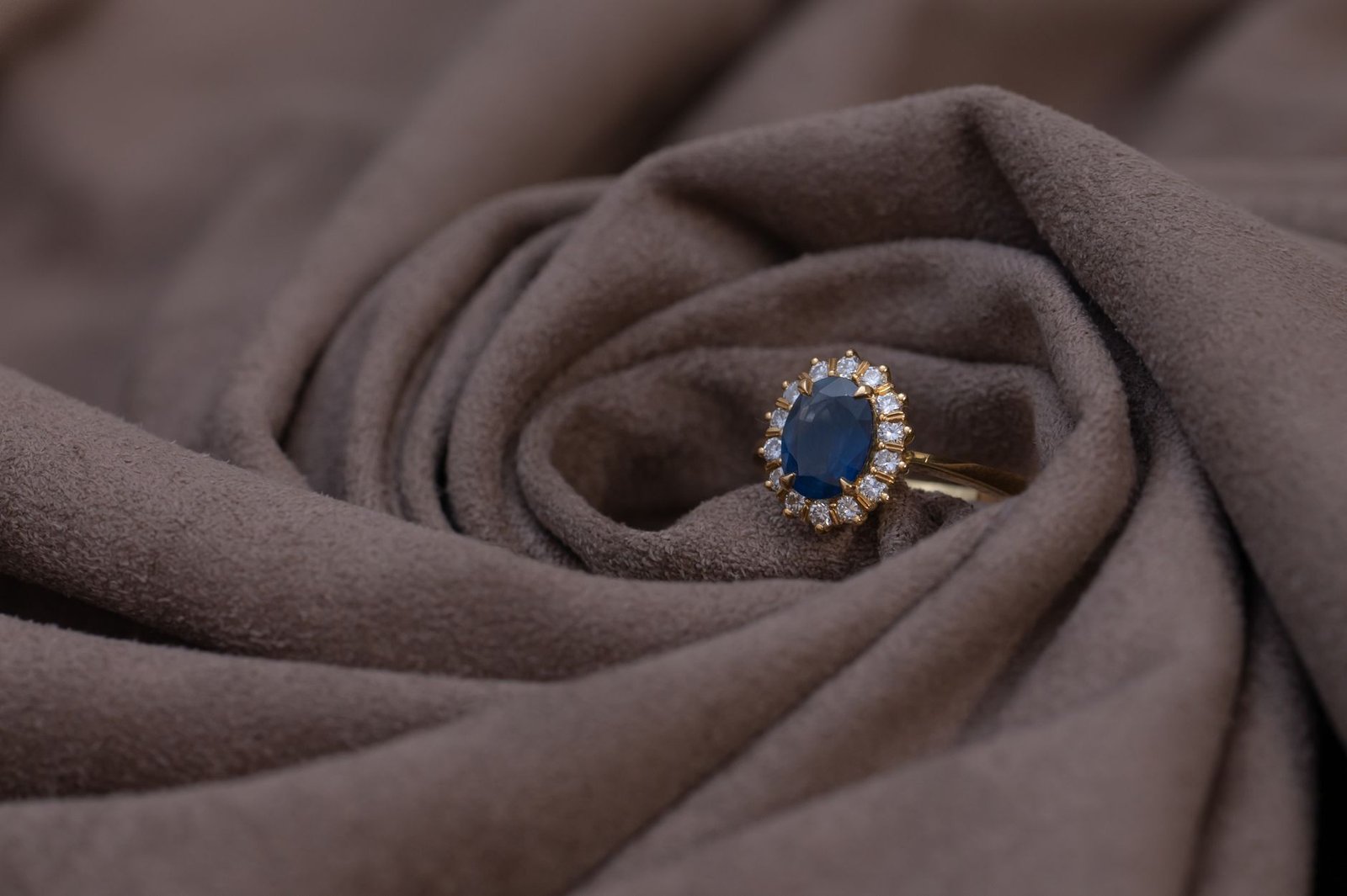 Close-up of a sapphire and diamond gold ring on brown suede, highlighting luxury jewelry details.